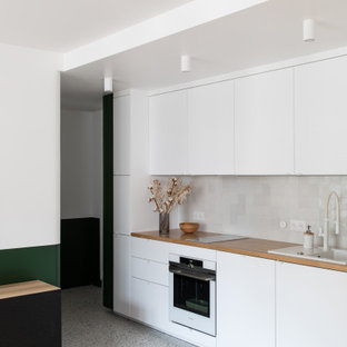 Diseño de cocina comedor lineal, contemporánea, pequeña, con fregadero de un seno, armarios con rebordes decorativos, puertas de armario blancas, encimera de madera, salpicadero blanco, salpicadero de azulejos de cerámica, electrodomésticos blancos, suelo de terrazo, suelo multicolor y encimeras beige