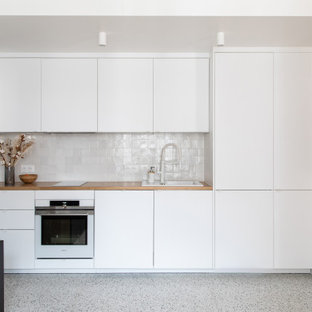 Ejemplo de cocina comedor lineal, actual, pequeña, con fregadero de un seno, armarios con rebordes decorativos, puertas de armario blancas, encimera de madera, salpicadero blanco, salpicadero de azulejos de cerámica, electrodomésticos blancos, suelo de terrazo, suelo multicolor y encimeras beige