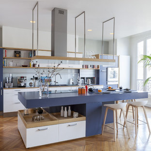 Cette image montre une cuisine design avec un placard à porte plane, des portes de placard blanches, une crédence blanche, une crédence en feuille de verre, un îlot central et un sol en bois brun.