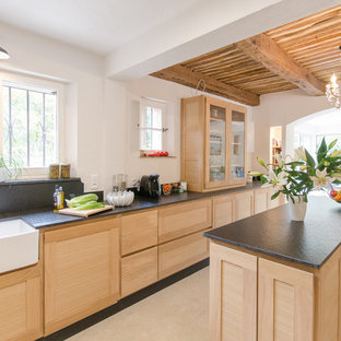Cette image montre une grand cuisine américaine méditerranéenne avec un évier de ferme, des portes de placard en bois clair, une crédence noire, un sol en carrelage de céramique, un îlot central, un sol beige et un placard à porte shaker.