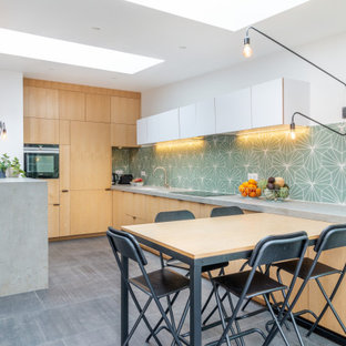 Exemple d'une cuisine ouverte tendance en U de taille moyenne avec un évier encastré, des portes de placard en bois clair, une crédence verte, un sol gris, un plan de travail gris, un placard à porte affleurante, un plan de travail en carrelage, une crédence en carreau de ciment, un électroménager noir, un sol en carrelage de céramique et un îlot central.