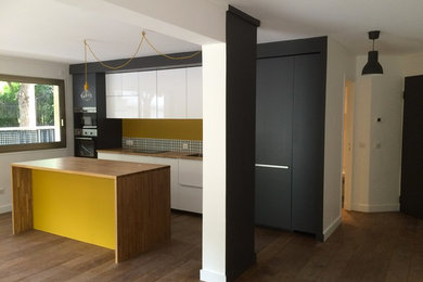 This is an example of a contemporary galley kitchen/diner in Paris with a submerged sink, white cabinets, wood worktops, yellow splashback, ceramic splashback, integrated appliances, light hardwood flooring and an island.