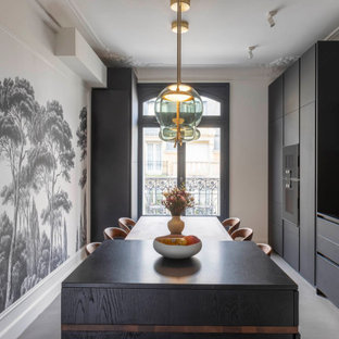 Aménagement d'une grand cuisine linéaire contemporaine fermée avec un évier encastré, des portes de placard noires, un plan de travail en granite, une crédence métallisée, un électroménager encastrable, béton au sol, un îlot central, un sol gris et un plan de travail noir.