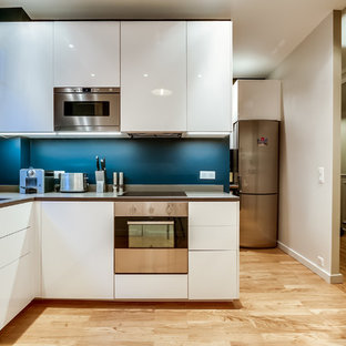 Aménagement d'une cuisine contemporaine en L fermée et de taille moyenne avec un évier encastré, un placard à porte plane, des portes de placard blanches, une crédence bleue, un électroménager en acier inoxydable, un sol en bois clair et aucun îlot.
