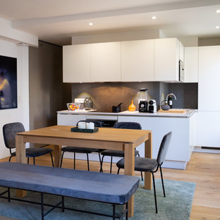 Idées déco pour une cuisine américaine contemporaine en L avec un évier encastré, un placard à porte plane, des portes de placard blanches, une crédence grise, un électroménager en acier inoxydable, un sol en bois brun, 2 îlots, un sol marron et un plan de travail blanc.