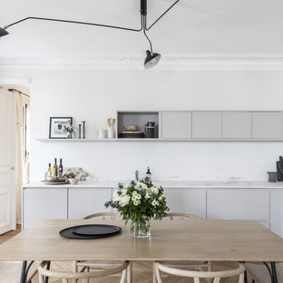 Idée de décoration pour une cuisine américaine nordique en L de taille moyenne avec des portes de placard grises, un plan de travail en quartz modifié, une crédence blanche, un électroménager noir, un sol en bois clair, aucun îlot, un plan de travail blanc et un placard à porte plane.