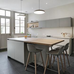 Aménagement d'une cuisine contemporaine en L de taille moyenne avec un évier intégré, un placard à porte plane, des portes de placard grises, une crédence beige, un électroménager encastrable, un sol en carrelage de porcelaine, un îlot central, un sol noir et un plan de travail beige.