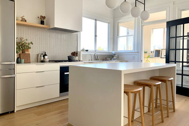 Inspiration for a mid-sized contemporary beige floor and light wood floor kitchen remodel in San Francisco with flat-panel cabinets, white cabinets, gray backsplash, ceramic backsplash, stainless steel appliances, an island, white countertops and an undermount sink