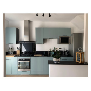 Idée de décoration pour une cuisine ouverte parallèle minimaliste de taille moyenne avec un évier encastré, un placard à porte plane, des portes de placards vertess, un plan de travail en granite, une crédence noire, une crédence en granite, un électroménager en acier inoxydable, un sol en bois clair, un îlot central, un sol marron, un plan de travail noir et un plafond en papier peint.