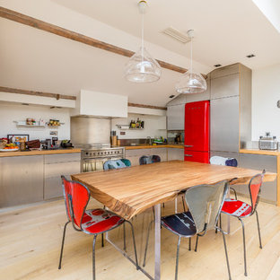 Idées déco pour une cuisine américaine industrielle en U avec un placard à porte plane, une façade en inox, un plan de travail en bois, une crédence métallisée, un électroménager de couleur, un sol en bois clair et un sol beige.