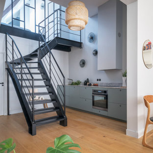 Cette image montre une cuisine ouverte linéaire urbaine de taille moyenne avec des portes de placard bleues, un plan de travail en granite, un électroménager en acier inoxydable, aucun îlot, un placard à porte plane, un sol en bois brun et un plan de travail gris.
