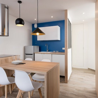 Exemple d'une cuisine américaine parallèle tendance avec un évier posé, un placard à porte plane, des portes de placard blanches, un plan de travail en bois, une crédence bleue, un électroménager en acier inoxydable, un sol en bois clair, une péninsule, un sol beige et un plan de travail beige.