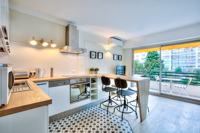 This is an example of a small contemporary u-shaped kitchen/diner in Nice with white cabinets, wood worktops, white splashback, ceramic splashback, cement flooring, a built-in sink, flat-panel cabinets, stainless steel appliances, a breakfast bar, multi-coloured floors and brown worktops.