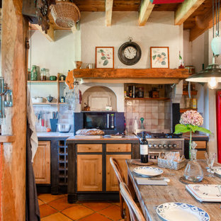 Cette image montre une cuisine américaine rustique en L avec un placard avec porte à panneau surélevé, des portes de placard en bois brun, un plan de travail en carrelage, un électroménager en acier inoxydable, un sol rouge et un plan de travail beige.