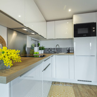 Cette image montre une cuisine design en L de taille moyenne avec un évier posé, des portes de placard blanches, un plan de travail en bois, une crédence métallisée, une crédence en dalle métallique, un électroménager noir, un sol en bois brun et aucun îlot.