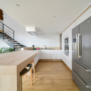 Réalisation d'une cuisine ouverte design en U de taille moyenne avec un évier posé, un placard à porte plane, des portes de placard blanches, un électroménager en acier inoxydable, une péninsule, un sol marron, un plan de travail beige, un plan de travail en bois, une crédence beige, une crédence en bois et un sol en bois foncé.