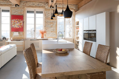 Cette image montre une cuisine ouverte méditerranéenne avec un évier 1 bac, un placard à porte plane, des portes de placard blanches, un électroménager noir, îlot, un sol gris et un plan de travail blanc.