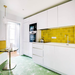 Exemple d'une cuisine ouverte linéaire tendance de taille moyenne avec un évier encastré, un placard à porte plane, des portes de placard blanches, un plan de travail en quartz, une crédence jaune, une crédence en carreau de terre cuite, un électroménager encastrable, un sol en carreaux de ciment, aucun îlot, un sol vert et un plan de travail blanc.