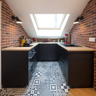 Inspiration pour une cuisine américaine nordique avec un évier posé, un placard à porte plane, des portes de placard noires, un plan de travail en bois, une crédence rouge, une crédence en brique, un électroménager noir, un sol en carreaux de ciment, un sol multicolore et un plan de travail marron.