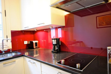 Inspiration for a medium sized contemporary l-shaped enclosed kitchen in Paris with a submerged sink, louvered cabinets, white cabinets, granite worktops, red splashback, glass sheet splashback, stainless steel appliances and no island.