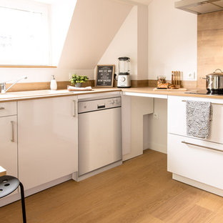 Cette photo montre une cuisine ouverte scandinave en L de taille moyenne avec un évier 1 bac, des portes de placard blanches, une crédence en bois, un électroménager en acier inoxydable, un placard à porte affleurante, un plan de travail en bois, une crédence beige, un sol en bois clair, un îlot central et un sol beige.