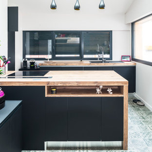 Réalisation d'une grand cuisine ouverte design en U avec un évier 2 bacs, un placard avec porte à panneau encastré, des portes de placard noires, un plan de travail en bois, un électroménager encastrable, un sol en carrelage de céramique et un îlot central.