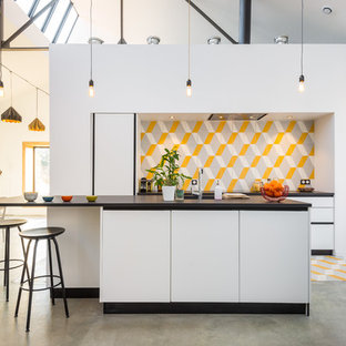 Cette photo montre une cuisine américaine parallèle tendance de taille moyenne avec une crédence en carreau de céramique, un îlot central, un placard à porte plane, des portes de placard blanches et une crédence multicolore.