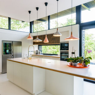 Aménagement d'une cuisine contemporaine en L avec un placard à porte plane, des portes de placard blanches, une crédence en fenêtre, un électroménager en acier inoxydable, un îlot central, un sol blanc, un plan de travail blanc, un évier encastré, un plan de travail en surface solide et béton au sol.