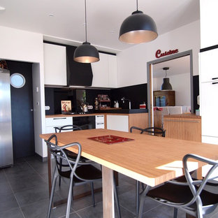 Cette image montre une cuisine minimaliste en L fermée et de taille moyenne avec un évier 2 bacs, un placard à porte affleurante, des portes de placard blanches, un plan de travail en bois, une crédence noire, une crédence en ardoise, un électroménager noir, un sol en carrelage de céramique, aucun îlot et un sol gris.