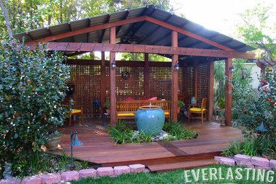 Example of a mid-sized classic backyard water fountain deck design in Miami with a roof extension