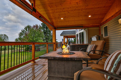 Large mountain style backyard deck photo in Seattle with a roof extension and a fire pit