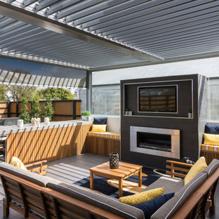 Réalisation d'une terrasse arrière design avec une cheminée et une pergola.
