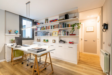 Diseño de despacho contemporáneo de tamaño medio con biblioteca, paredes beige, suelo laminado, suelo marrón y escritorio independiente