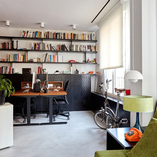 Foto på ett stort funkis arbetsrum, med ett bibliotek, vita väggar, betonggolv, ett fristående skrivbord och grått golv