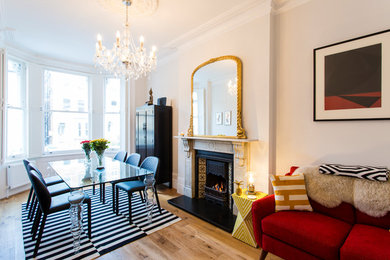 Inspiration for a medium sized eclectic dining room in London with beige walls, light hardwood flooring, a standard fireplace, a stone fireplace surround and beige floors.