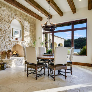 Ispirazione per una sala da pranzo mediterranea con pareti bianche, camino classico, cornice del camino in pietra e pavimento beige