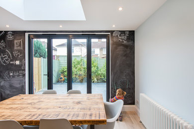 This is an example of a small contemporary open plan dining room in London with black walls, light hardwood flooring, no fireplace and beige floors.