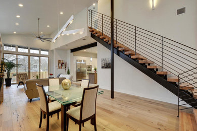 Cette photo montre une grande salle à manger ouverte sur le salon tendance avec un mur blanc, un sol en bois brun et aucune cheminée.