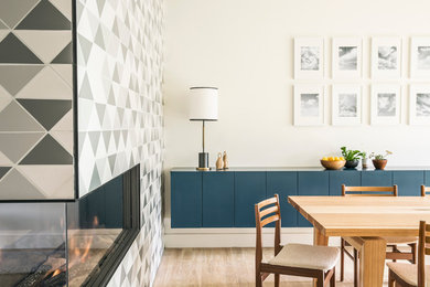 Diseño de comedor contemporáneo de tamaño medio con paredes blancas, suelo de madera clara, chimenea de doble cara, marco de chimenea de baldosas y/o azulejos y suelo beige