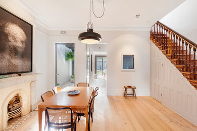 Scandi dining room in Sydney with light hardwood flooring, white walls and a standard fireplace.