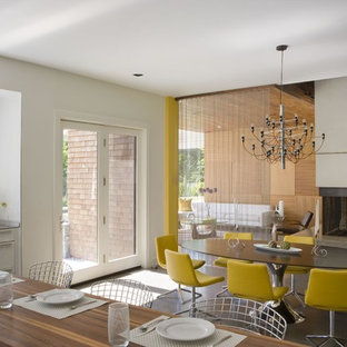 Idee per una grande sala da pranzo aperta verso la cucina contemporanea con pavimento in cemento, pareti bianche, camino bifacciale e cornice del camino in cemento