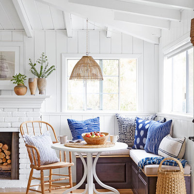 Example of a small beach style light wood floor dining room design in Los Angeles with white walls, a standard fireplace and a brick fireplace