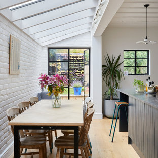 Idee per una sala da pranzo aperta verso la cucina minimal con pareti bianche, parquet chiaro, pavimento beige e pareti in mattoni