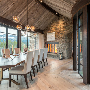 Foto di una sala da pranzo stile rurale con pareti grigie, parquet chiaro, camino bifacciale, cornice del camino in pietra e pavimento beige