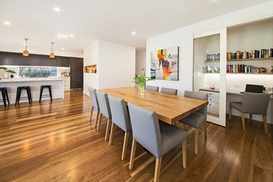 Cette photo montre une salle à manger ouverte sur le salon tendance avec un mur blanc et un sol en bois brun.