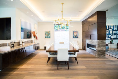 Inspiration for a large contemporary medium tone wood floor and brown floor dining room remodel in Los Angeles with white walls, a two-sided fireplace and a stone fireplace