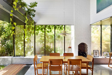 Cette photo montre une salle à manger ouverte sur le salon tendance de taille moyenne avec un mur blanc, sol en béton ciré, une cheminée standard, un manteau de cheminée en brique et un sol gris.