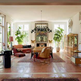Foto di una grande sala da pranzo aperta verso il soggiorno boho chic con pareti bianche, pavimento in terracotta, camino classico, cornice del camino in intonaco e pavimento arancione
