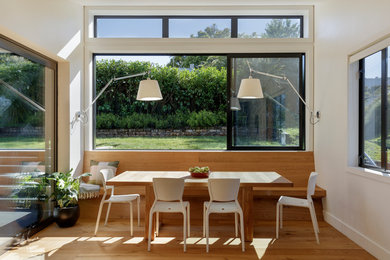 Cette image montre une salle à manger ouverte sur la cuisine design avec un mur blanc et un sol en bois brun.