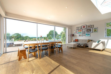 This is an example of a large contemporary open plan dining room in Sussex with white walls, light hardwood flooring and brown floors.